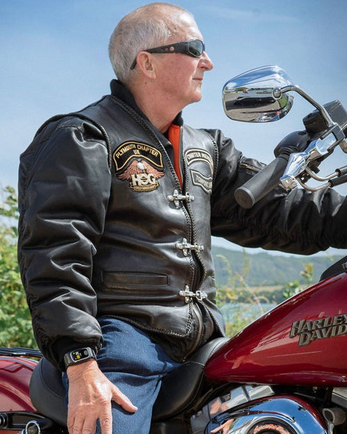 Man wearing a personal alarm watch on a motorcycle, with a scenic background.