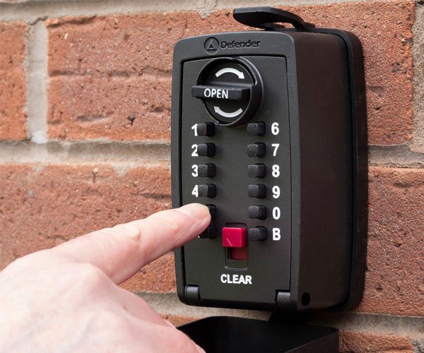 Hand pressing a key safe on a brick wall.