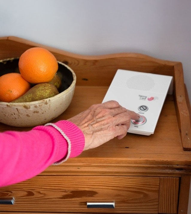 A close-up of a person's hand in a pink sleeve pressing buttons on an alarm base unit