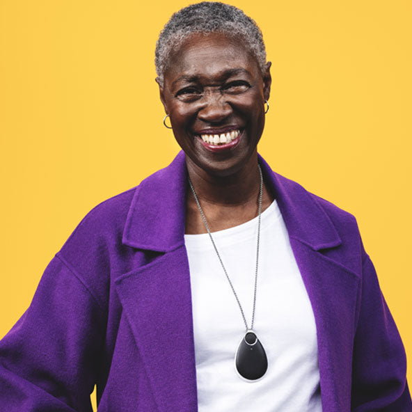 A smiling woman with short gray hair wearing a bright purple coat wearing a personal alarm